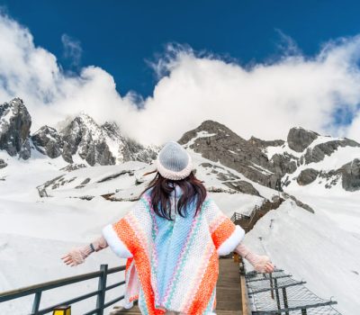 Persona contemplando un paisaje de montañas nevadas desde una pasarela panorámica en el Parque Nacional de la Montaña Nevada del Dragón de Jade, China.